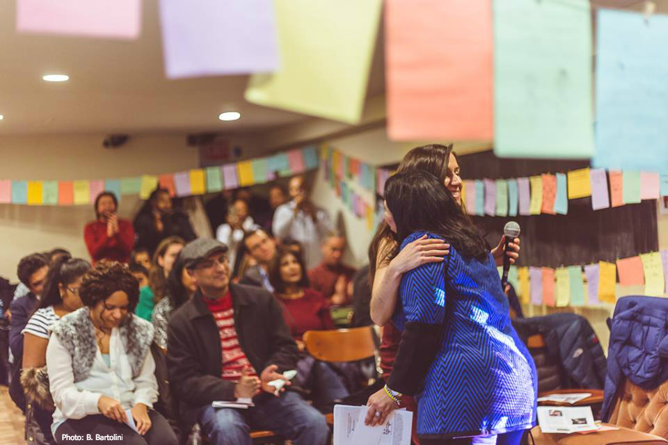 Photo of Bridget Bartolini and Wendy Angulo hugging in front of a full audience