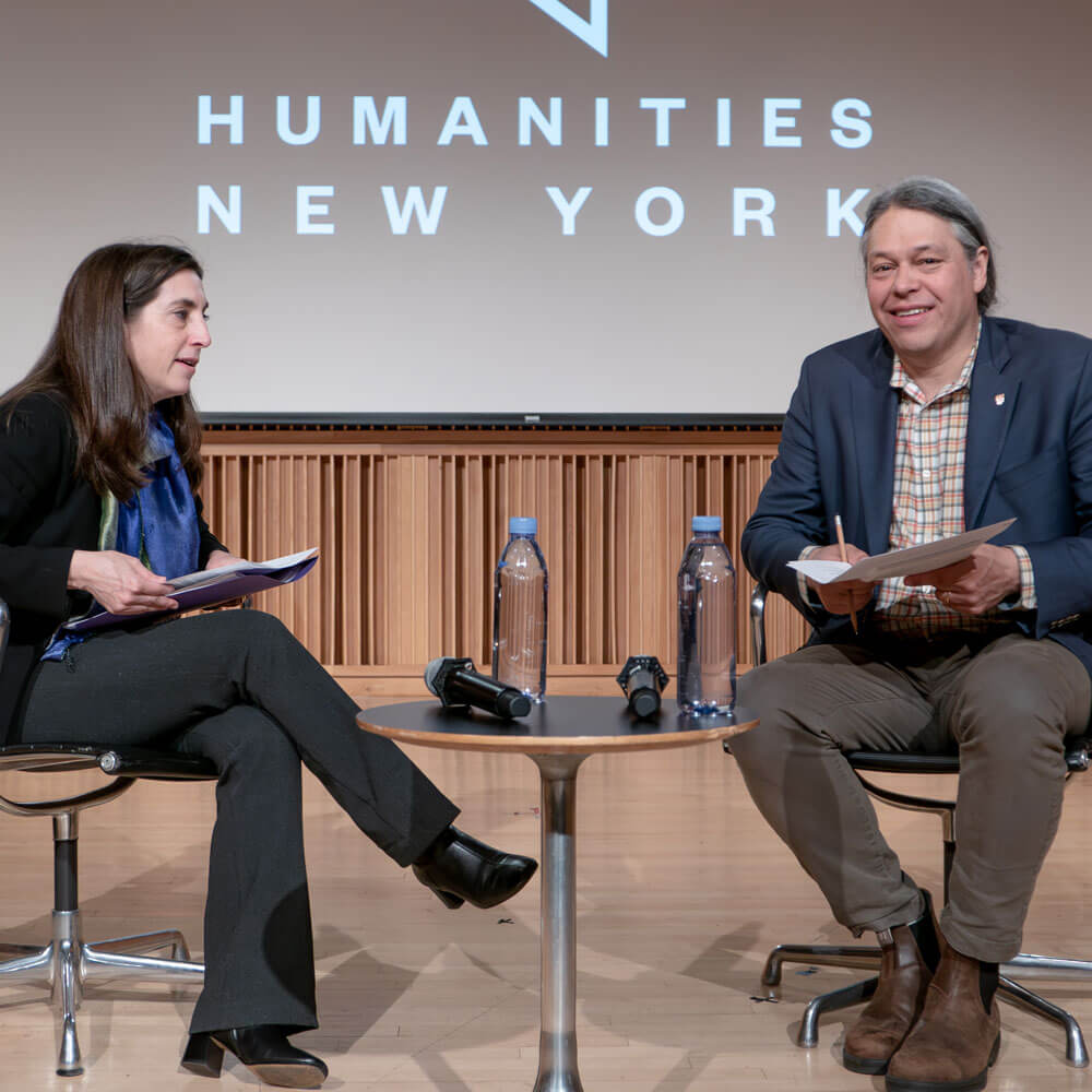 a man and a woman sit on stage presenting, and interviewing one another