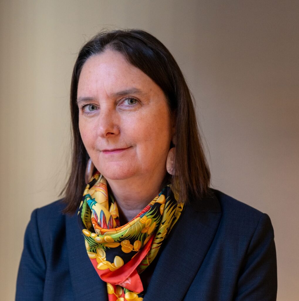 Head and shoulders of executive director Sara Ogger, wearing blue blazer and red printed scarf