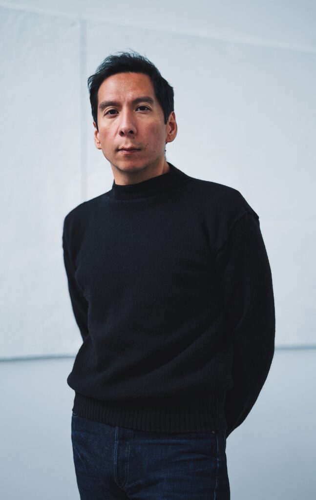 Indigenous artist Sky Hopinka in a black turtleneck against a slate-grey background