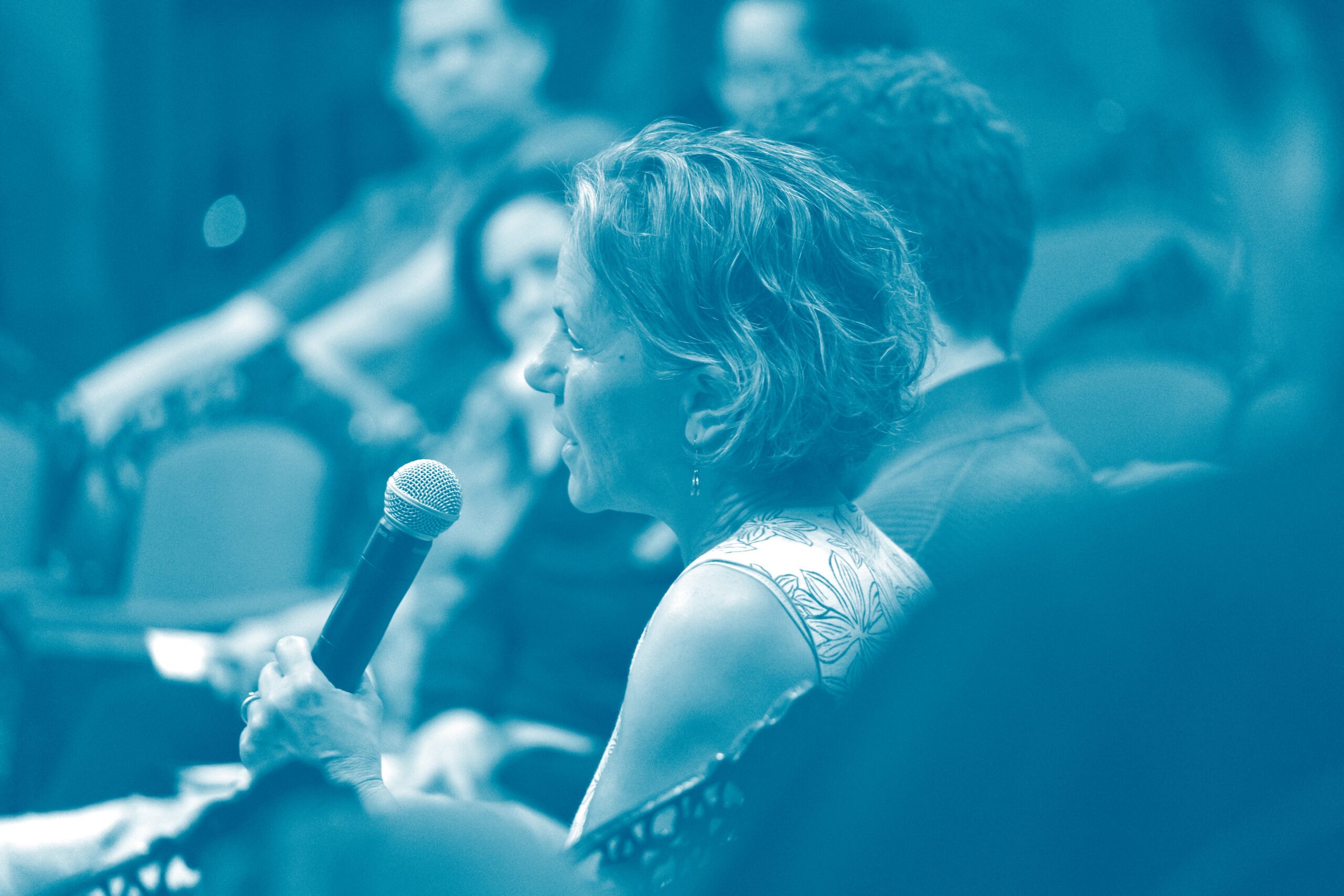 Woman with short hair speaking into microphone in auditorium.